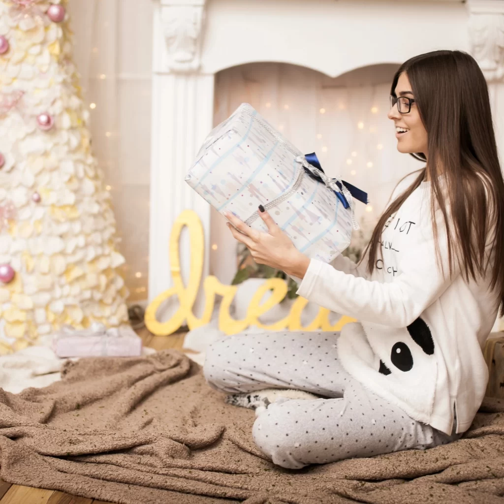 Woman sitting on floor opening a wrapped holiday gift.