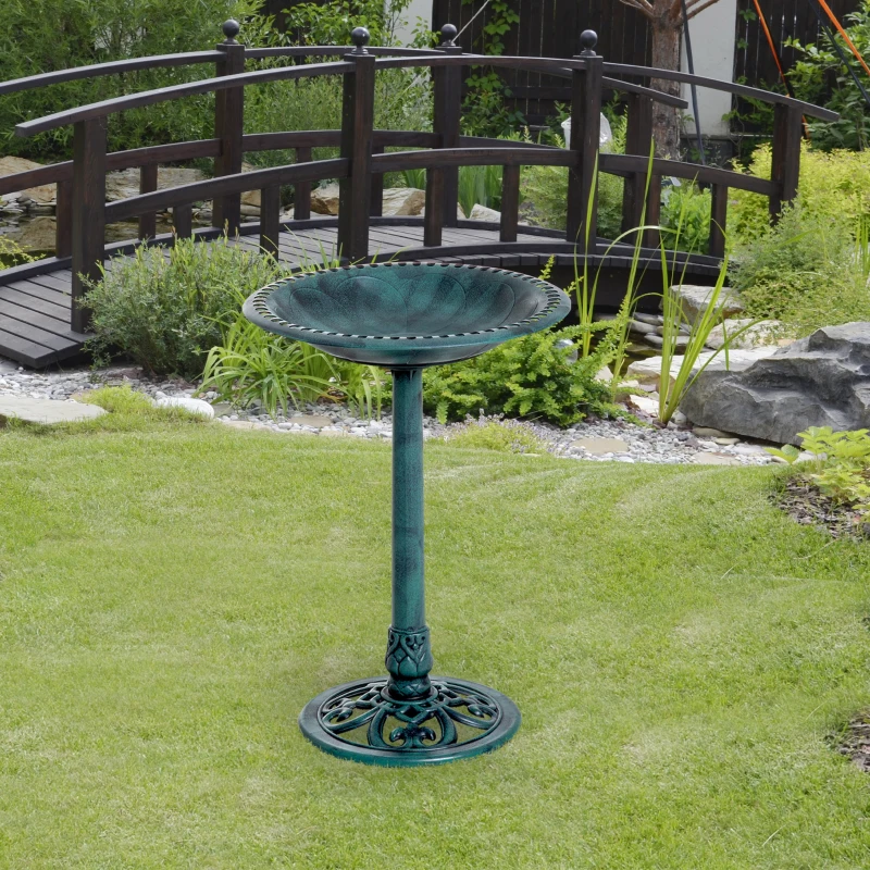 Ornate green bird bath in a garden setting with a bridge.