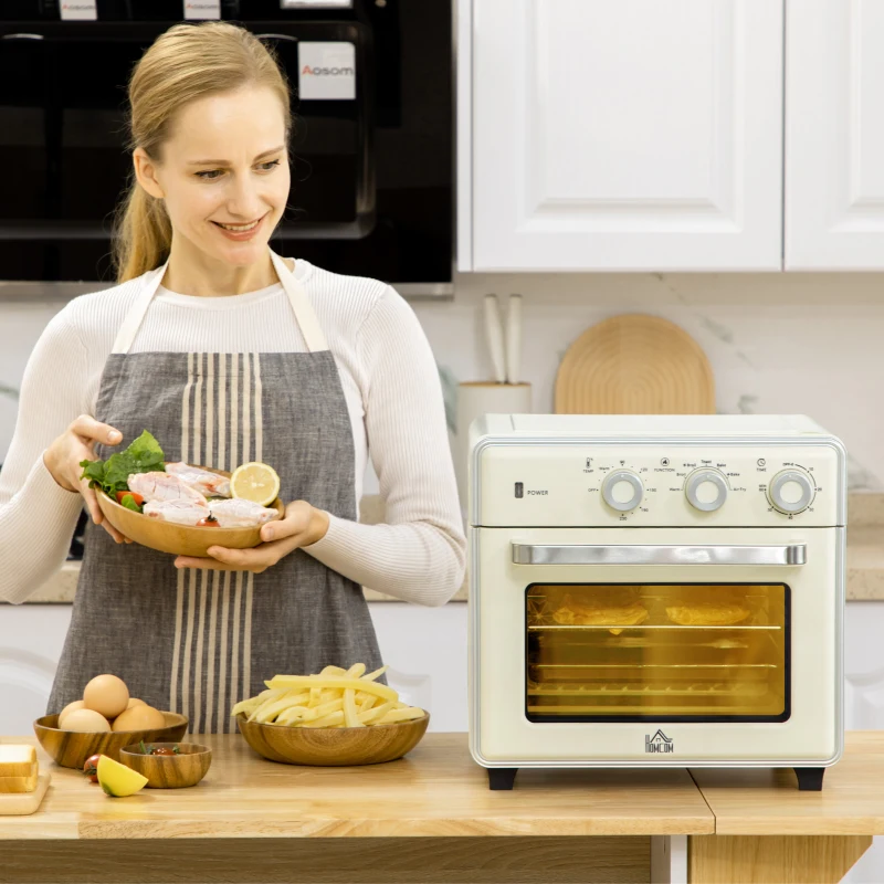 Compact white air fryer oven in white kitchen beside bread, fruits, and cooking utensils.
