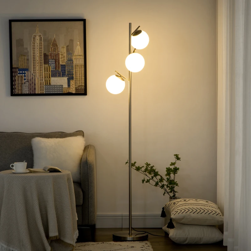 Silver floor lamp with three glowing round bulbs beside a sofa in a cosy room.
