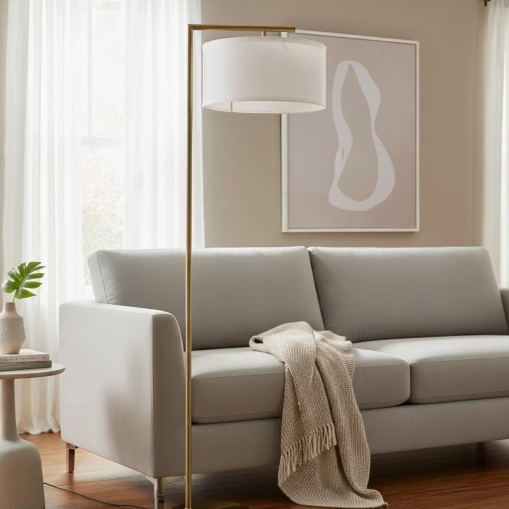 Gold standing lamp with white drum shade beside a light grey sofa.