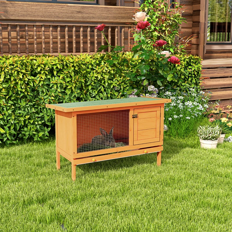 Small wooden rabbit hutch on grass with a rabbit resting inside.
