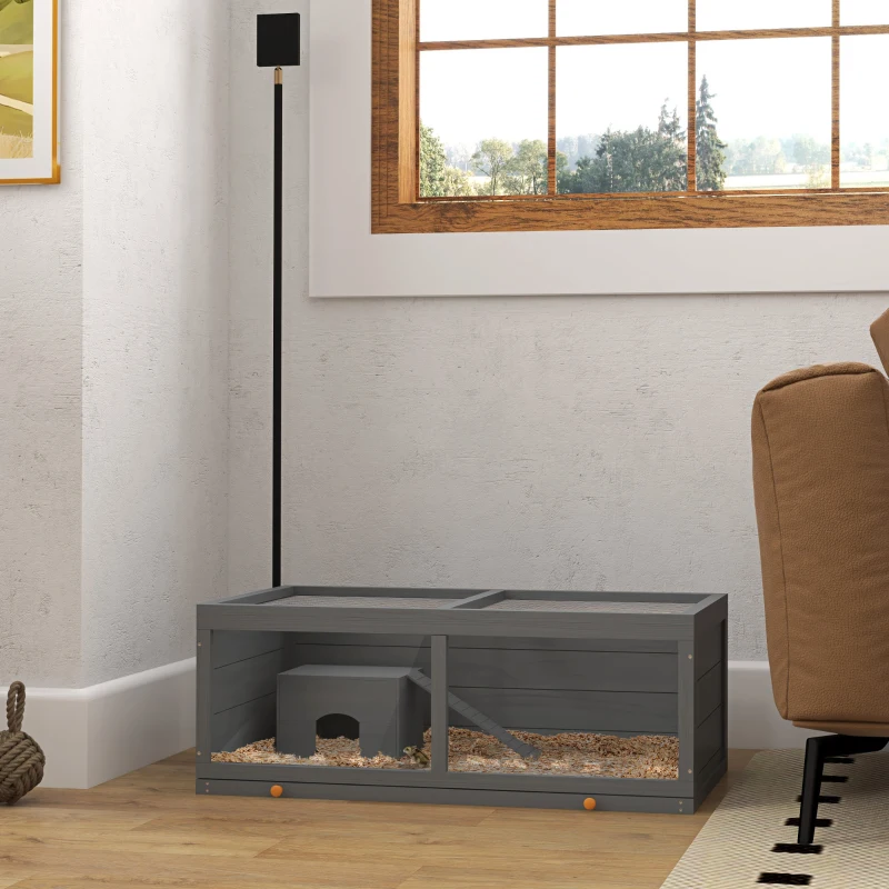 Low, gray wooden cage on floor with deep bedding and small house inside.

