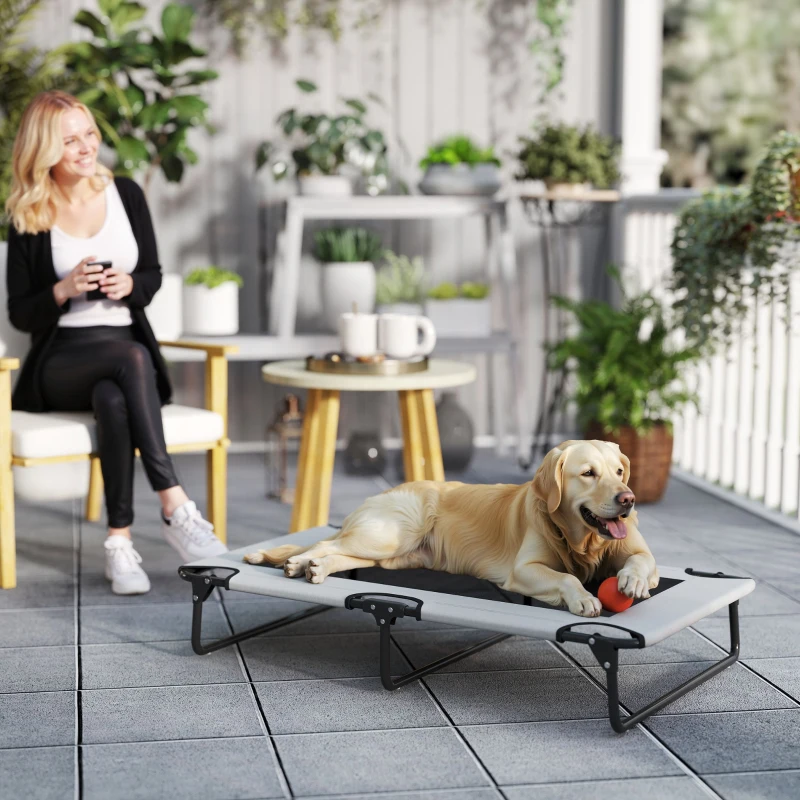 Golden retriever lying on raised outdoor cot beside woman on patio.
