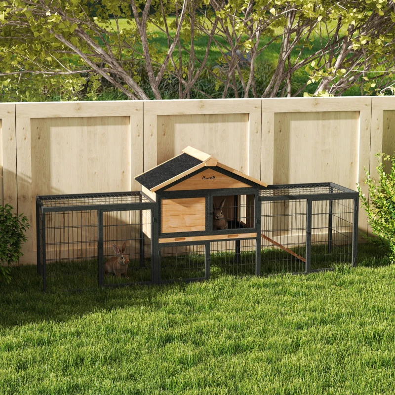 Large wooden rabbit house with extended steel run and rabbits sitting on grass.

