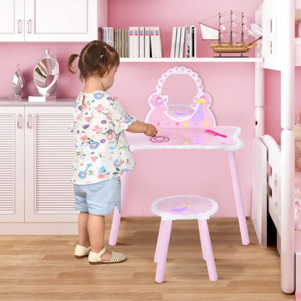 Young child interacting with a pink vanity table and stool set in a decorated bedroom.
