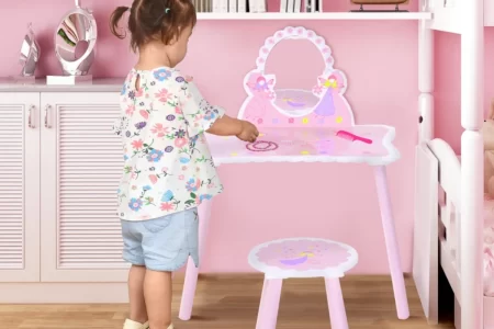Young child interacting with a pink vanity table and stool set in a decorated bedroom.