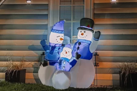 Inflatable snowman family glowing outside a house at night.